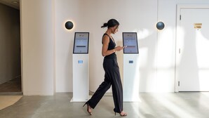 A woman walking past self-check-in kiosks in a hotel lobby.