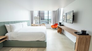 A modern hotel room with a large bed, a desk, a chair, and a TV mounted on the wall.