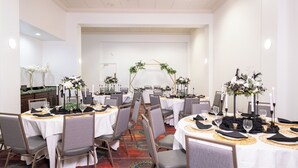 A banquet hall with round tables, grey chairs, white tablecloths, and floral centerpieces.