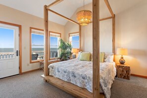 A bedroom with a four-poster bed, large windows, a view of the ocean, and a wooden ceiling.