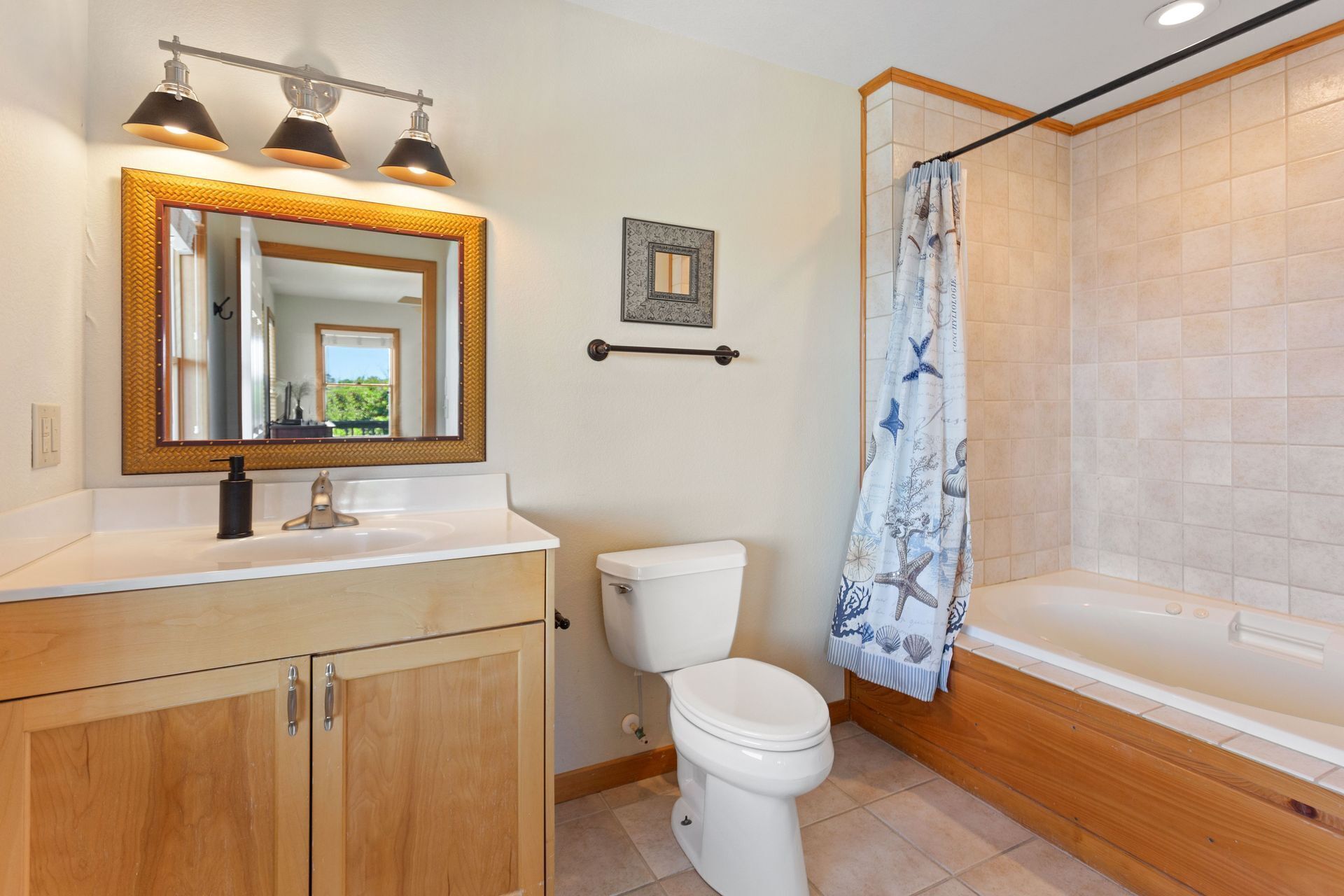 A bathroom with a wooden vanity, a white toilet, a bathtub, and a shower curtain with a marine theme.