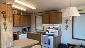 A compact kitchen with wooden cabinets, a stove, and a dining area with a table and chairs. - #1 Greenside Oasis (Mattawa)