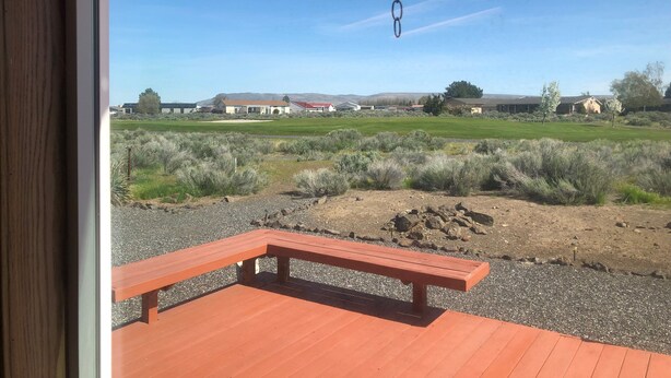 A wooden deck with a bench, a hanging chain, and a view of a rural landscape with houses and fields. - #1 Greenside Oasis (Mattawa)