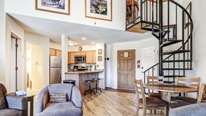 A spacious living area with a kitchen, a dining table with chairs, and a spiral staircase.