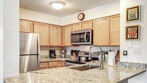 A kitchen with wooden cabinets, stainless steel appliances, granite countertops, and a clock on the wall.