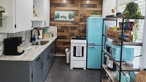 Une cuisine compacte avec un mur d’accent en bois, une cuisinière blanche, un réfrigérateur bleu et une étagère intégrée où sont rangées des collations.
