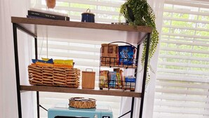 Une cuisine avec un four à micro-ondes GIALANZ bleu, un grille-pain et une machine à café, le tout posé sur une étagère en bois. On aperçoit des en-cas et un panier sur l’étagère du haut, ainsi qu’une plante sur la droite.