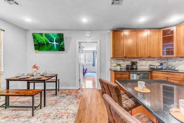A modern kitchen with wooden cabinets, a black countertop, and a dining area with a wooden table and chairs.