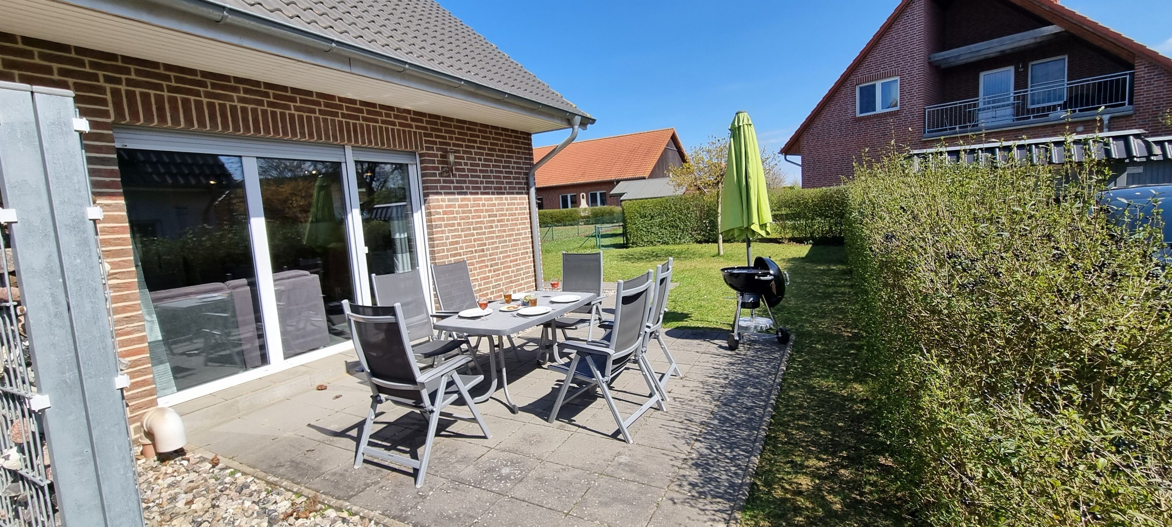 Une terrasse avec une table et des chaises, un barbecue et un parasol vert.