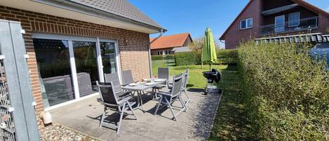 Une terrasse avec une table et des chaises, un barbecue et un parasol vert.
