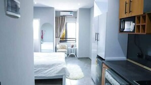 Ein kleines Hotelzimmer mit Bett, einer Sitzecke, einer Küchenzeile und einem fenster mit Vorhängen.