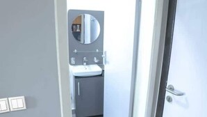 Ein schmaler Flur, der zu einem Badezimmer mit Waschbecken, Spiegel und Schränken führt.