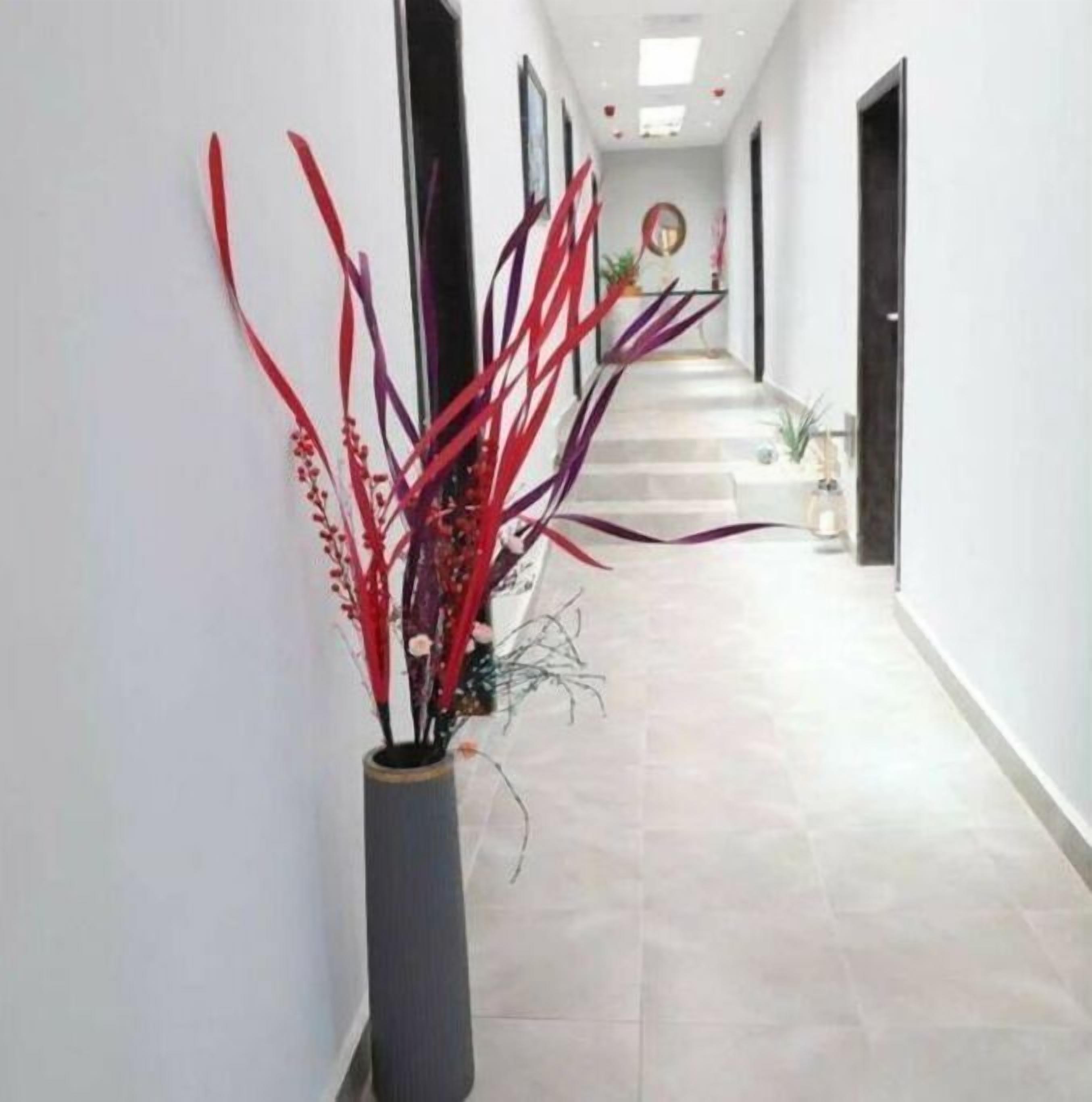 A hallway with a vase of red and purple decorative plants, a staircase, and a door on the right.