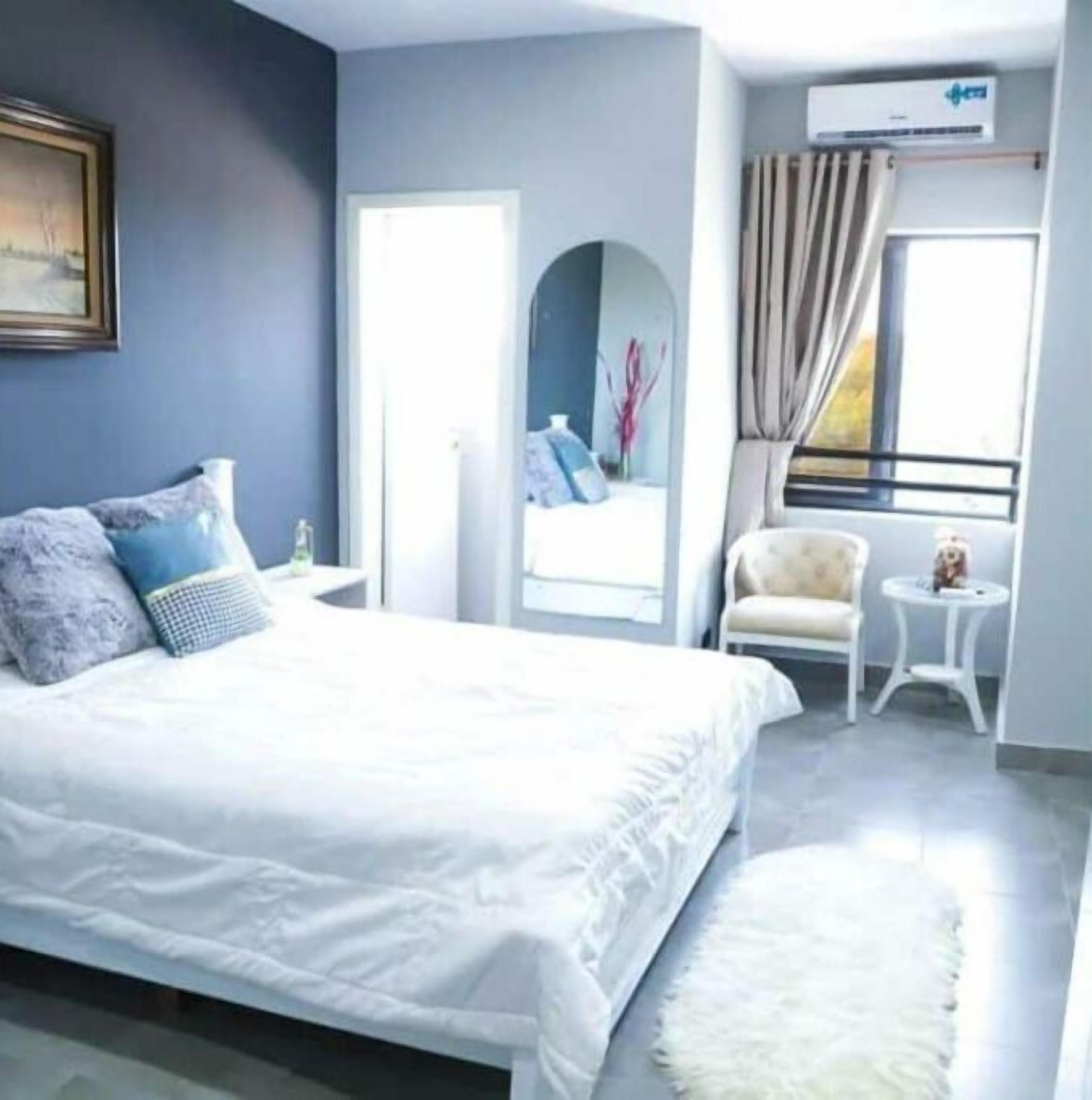 Um quarto moderno com uma cama grande, uma mesinha de cabeceira, uma cadeira e uma janela com cortinas.