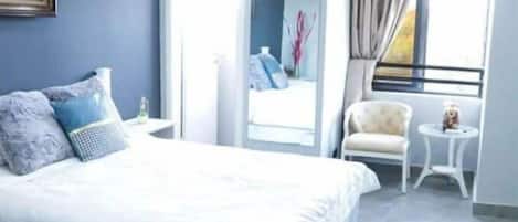A modern bedroom with a large bed, a small side table, a chair, and a window with curtains.