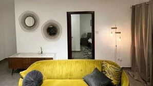 Ein Zimmer mit einem gelben Sofa, einem kleinen Tisch und einem Spiegel an der Wand.