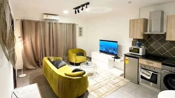 Ein modernes Wohnzimmer mit gelbem Sofa, Flachbildfernseher und einer Küchenzeile.