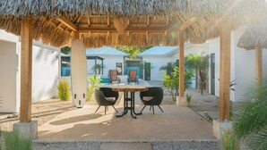 Un patio exterior con techo de paja, una mesa y dos sillas.