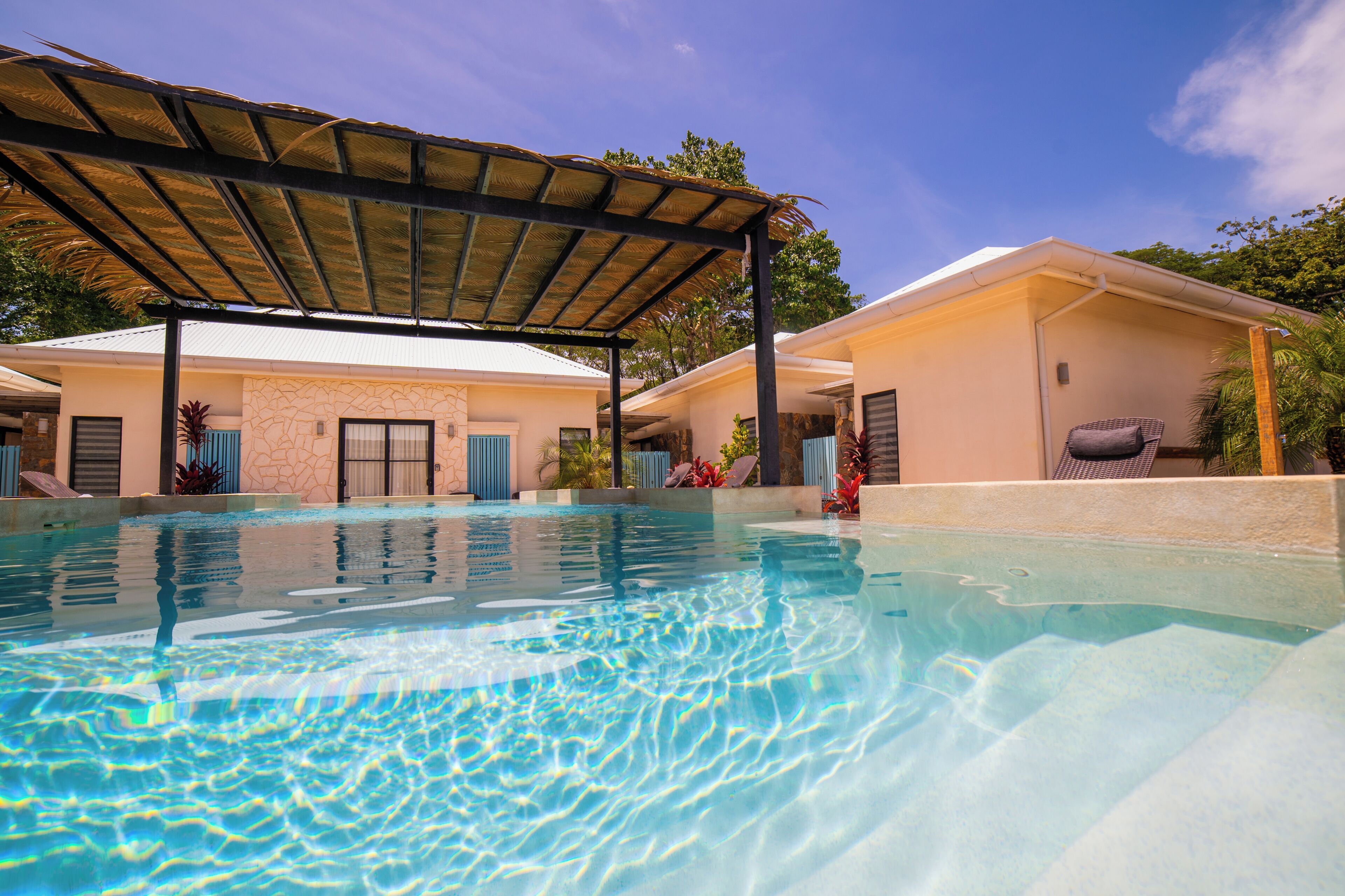 A swimming pool with a covered area, a building with a stone facade, and a clear blue sky.