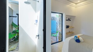 Un baño moderno con ducha, un vidrio que da a un patio, y una cama con una toalla y una toalla enrollada.