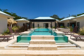 Un espace piscine avec des marches menant à l’eau, des chaises longues et des structures abritées.