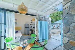Un espace repas extérieur moderne, avec une table en verre et des chaises vertes, un mur en pierre et une vue sur le jardin.