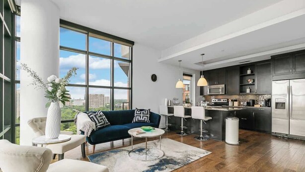 Una sala de estar moderna con un sofá, una mesa de centro y vistas a la ciudad a través de amplios ventanales.