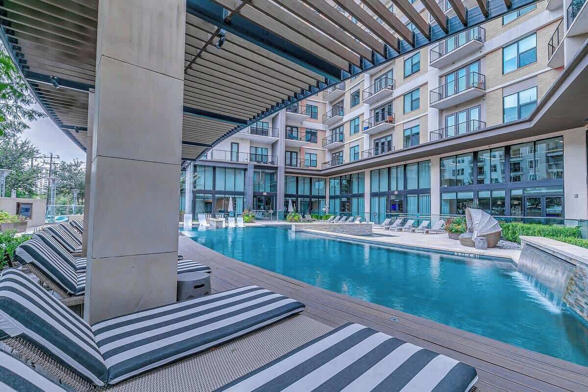 Ett modernt hotell med en swimmingpool, solstolar och ett takförsett område med utsikt över byggnadens fasad.