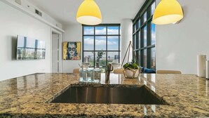 Una cocina moderna con encimeras de granito, una isla central, iluminación colgante y vistas a la ciudad a través de grandes ventanales.