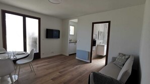 A modern living room with a dining area, a TV mounted on the wall, and a view into the kitchen. - Bas de Villa au Calme (Villeneuve-Loubet)