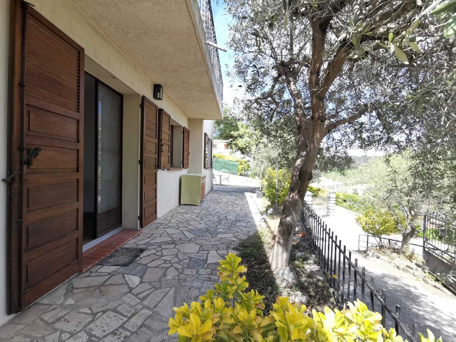 A building with a stone-paved entrance, wooden doors, and a tree-lined pathway.