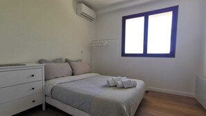 A bedroom with a bed, a white dresser, an air conditioning unit, and a window with blinds. - Bas de Villa au Calme (Villeneuve-Loubet)