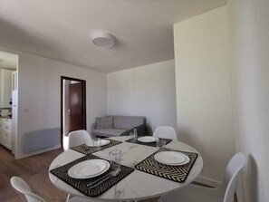 A dining area with a round table set for four, white chairs, and a grey sofa in the background.