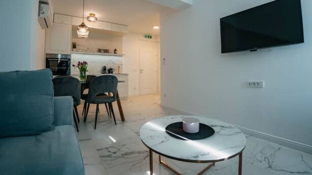 A modern living room with a sofa, a dining table with chairs, a kitchen in the background, and a flat-screen TV mounted on the wall. - Boutique Apartments Imotski 2 (Imotski)