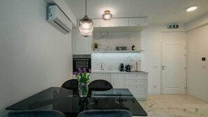 A modern kitchen with white cabinets, a marble countertop, and a dining area with a glass table and blue chairs. - Boutique Apartments Imotski 2 (Imotski)