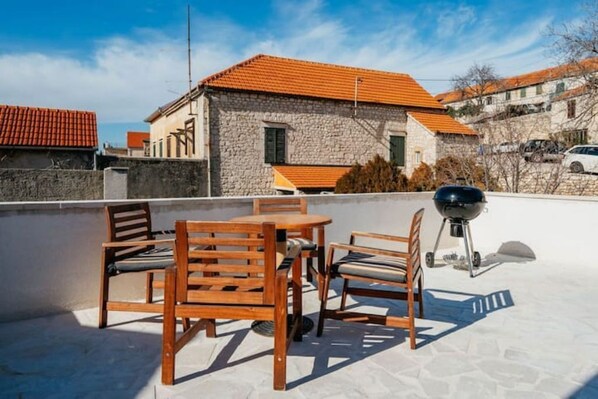 A rooftop terrace with a stone building, a barbecue grill, and wooden furniture. - Boutique Apartments Imotski 2 (Imotski)