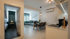 A modern hotel room with a bed, a small sitting area with a sofa and chairs, a dining table with chairs, and a kitchen area with a stove and microwave. - Boutique Apartments Imotski 2 (Imotski)