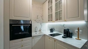 A kitchen with white cabinets, a black oven, a sink, and a countertop with a coffee maker and kettle. - Boutique Apartments Imotski 3 (Imotski)