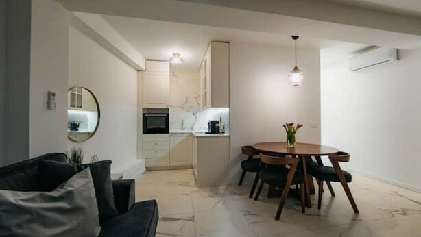 A modern living room with a dark-colored sofa, a round wooden dining table with four chairs, and a kitchen in the background. - Boutique Apartments Imotski 3 (Imotski)