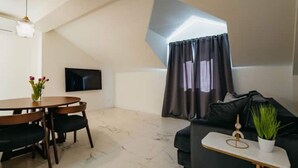 A modern living room with a dining area, a black sofa, a small table with a plant, and a TV mounted on the wall. - Boutique Apartments Imotski 3 (Imotski)