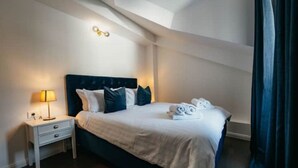 A neatly made bed with white linens and dark pillows, a bedside table with a lamp, and a window with curtains. - Boutique Apartments Imotski 3 (Imotski)