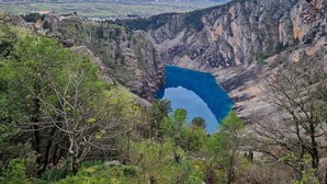 A valley with a clear blue lake surrounded by rocky cliffs and sparse vegetation. - Boutique Apartments Imotski 3 (Imotski)