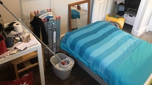 A bedroom with a bed, a desk with various items, a mirror, and a door leading to another room. - Studio with a view, great transport links to central London (London)