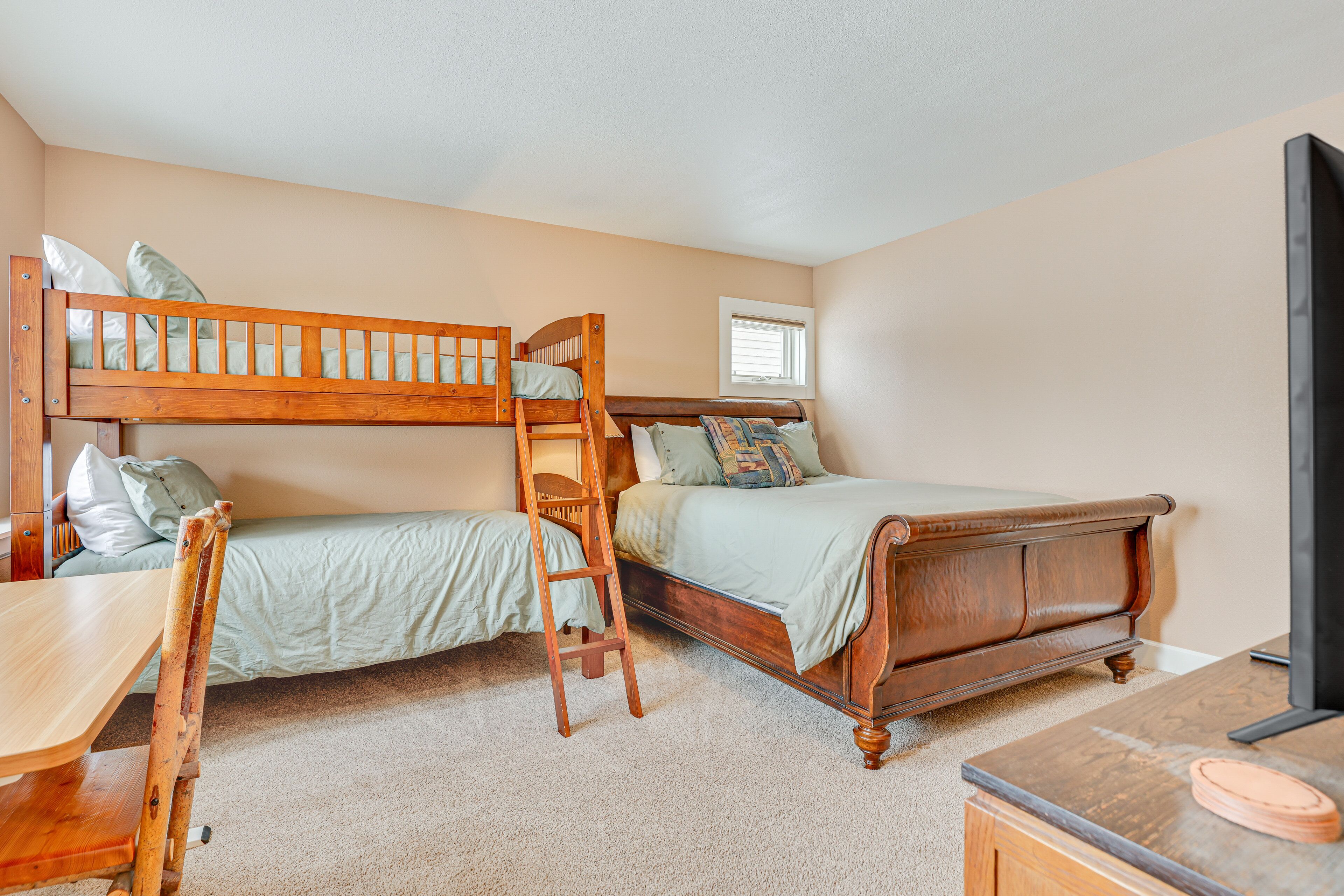 A bedroom with two bunk beds, a wooden desk, a chair, a ladder, a television, and a window.