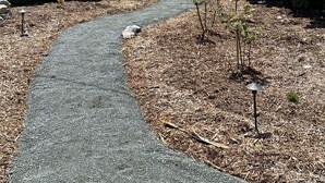 Un chemin menant à une maison avec une clôture bleue et un jardin parsemé de fleurs roses.