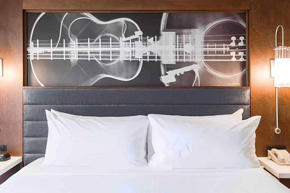 Een hotelkamer met een groot bed, een hoofdeinde met kunstwerk op het thema gitaar en bedlampjes.