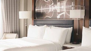 Een hotelkamer met twee bedden, een groot kunstwerk van een gitaar, een stoel en een lamp.