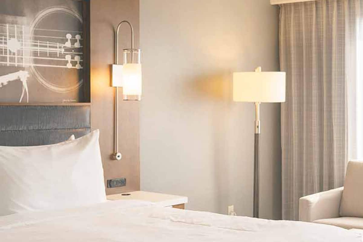 Een hotelkamer met een groot bed, een nachtkastje, een bureau, een stoel en een schilderij aan de muur.
