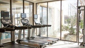 Een sportschool met loopbanden, fitnessapparatuur en grote ramen met uitzicht op het buitenland.