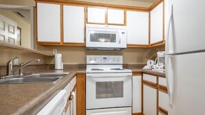 Una cocina con armarios blancos, microondas, estufa y refrigerador.